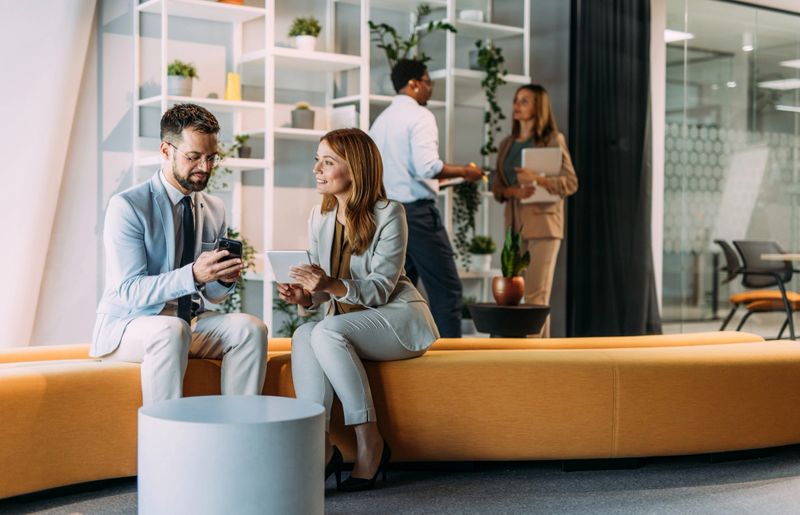 Shot of two coworkers having a discussion in modern office . Businessman and businesswoman in meeting using digital tablet and discussing business strategy while their colleagues working in background. Confident business people working together in the office. Creative business persons discussing new project and sharing ideas in the workplace.