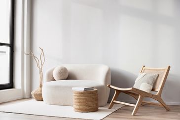 Minimalist living room with a cozy sofa, wooden chair, and round wicker table.