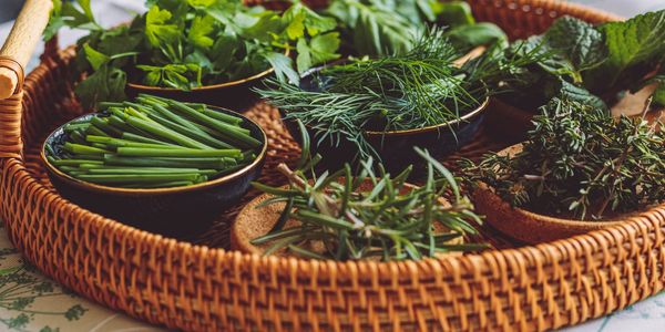 Variety of fresh herbs in bowls on a wicker tray.