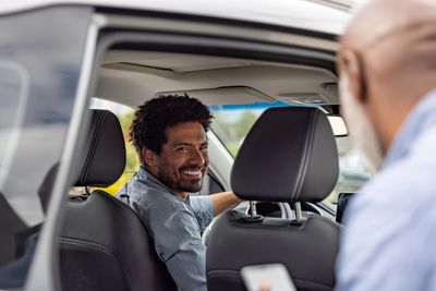 Man smiling in car while talking to person outside.