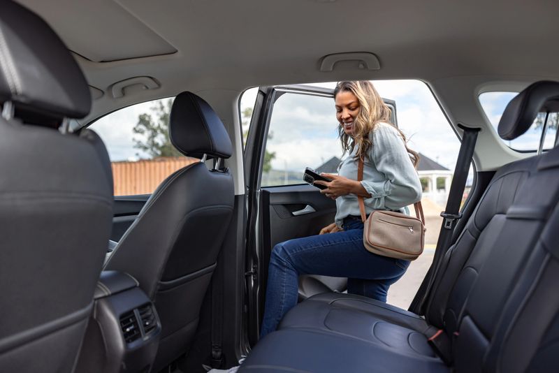 Latin American woman boarding a crowdsourced taxi holding her cell phone and smiling - mobility as a service concepts