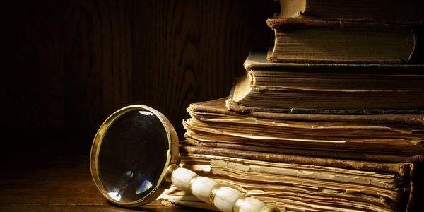 A vintage magnifying glass rests beside a stack of old, worn books.