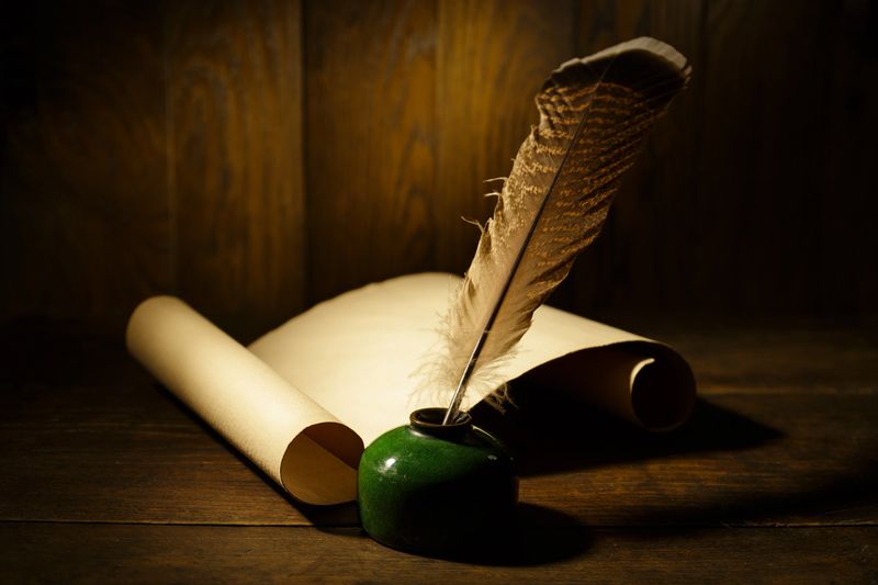 Ancient paper scroll with feather on old wooden table. Feather for calligraphy, old education, vintage fonts.