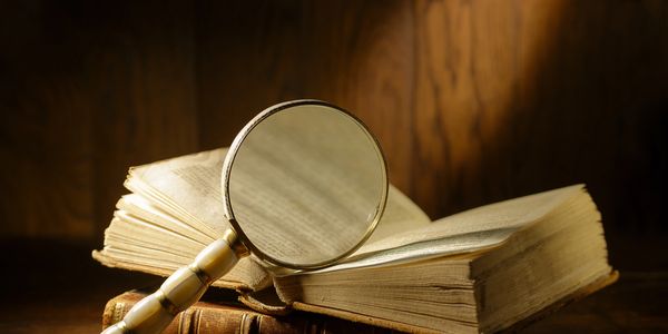 A magnifying glass resting on an open old book with wooden background.