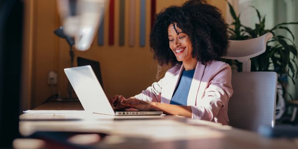 Smiling woman working on a laptop at a desk in a cozy office.