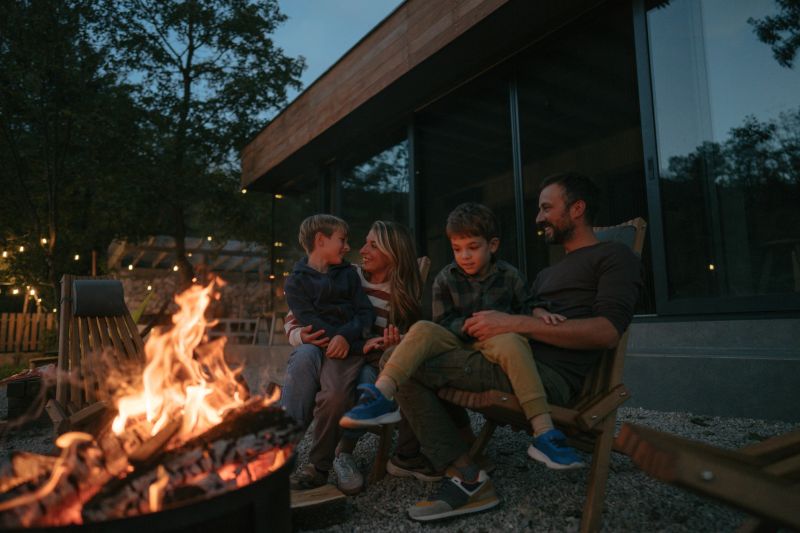 Photo of a young, loving family spending quality time together at the end of the busy week by the campfire in front of their vacation home.