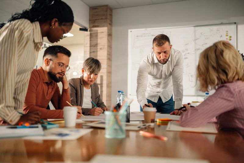 Diverse professionals collaborate in a modern office, led by their manager in a brainstorming session