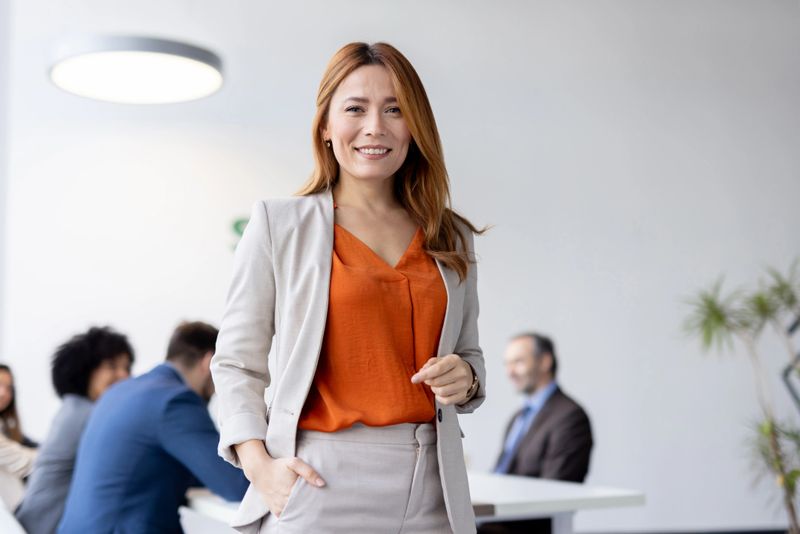 A confident woman in professional attire smiles broadly while giving a thumbs up in a stylish office, embodying positivity and teamwork.