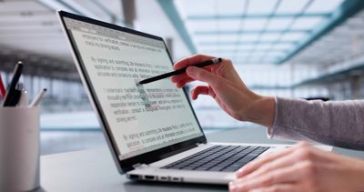 Person pointing at text on a laptop screen with a pen.