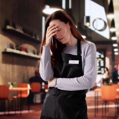 Stressed female barista in a cafe holding her forehead.
