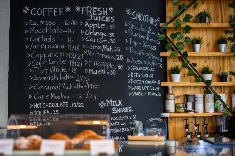 Interior shot of a small coffee shop with a chalkboard menu, pastry display, and green plants. Cozy food and drink establishment during the day.