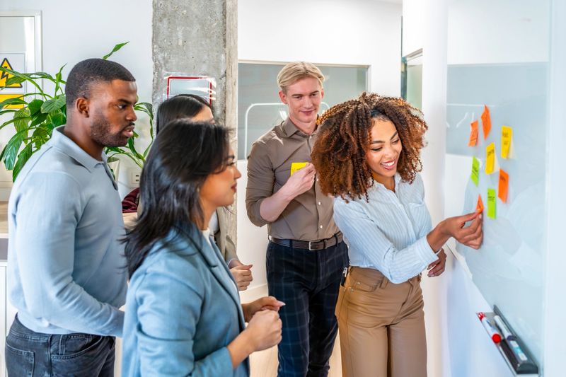 Group of young businesspeople sharing ideas in the office during a productive meeting, using colorful sticky notes on a whiteboard