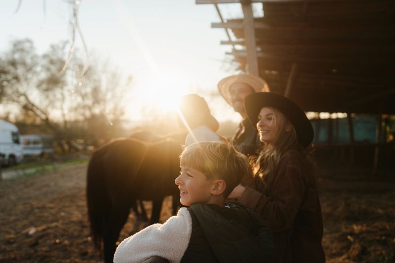 Photo of young family at their horse ranch, tending to their animals, while their two young boys are playing around.