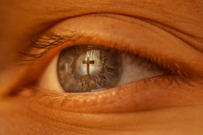 Close-up of eye reflecting a cross symbol.