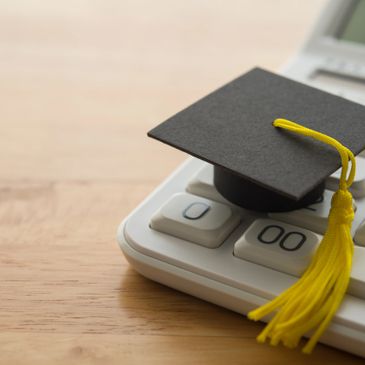 A small graduation cap resting on a calculator's buttons.