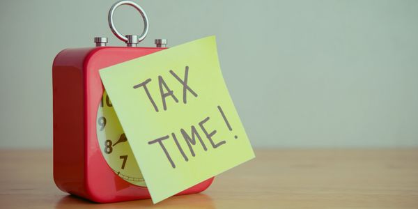 Red clock with a sticky note saying 'TAX TIME!' on a wooden surface.