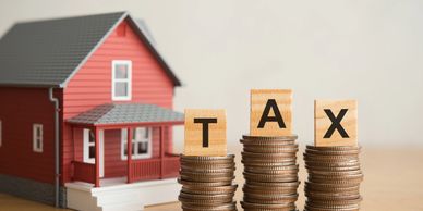 Coins stacked with blocks spelling TAX near a house model.