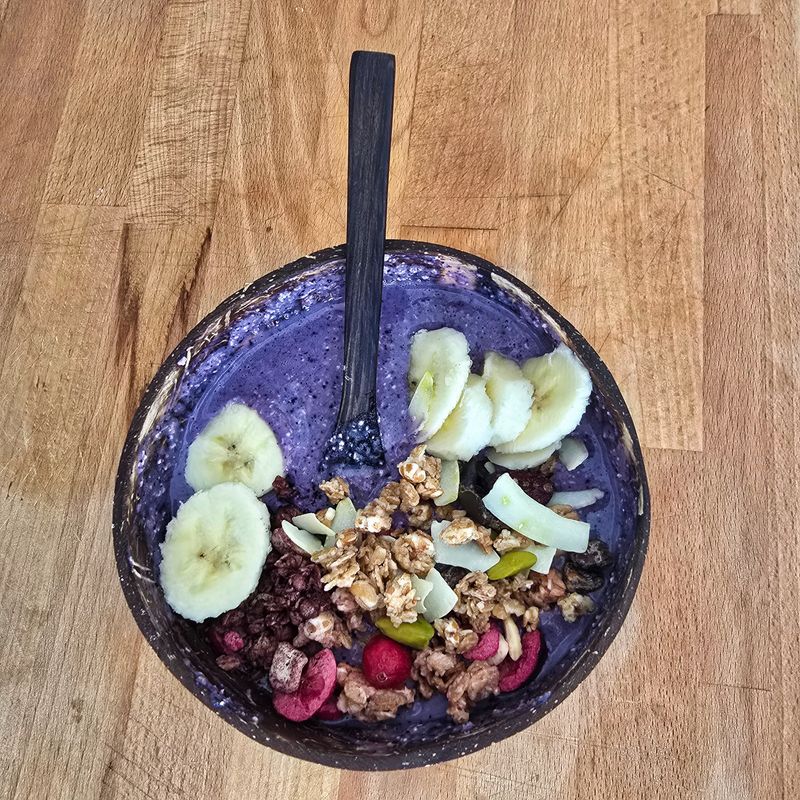 A colorful smoothie bowl topped with fresh banana slices, crunchy granola, and assorted mixed fruits