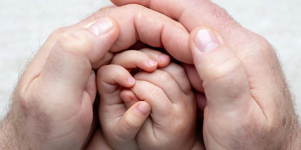 Adult hands gently encircle a child's hands symbolizing care and protection.