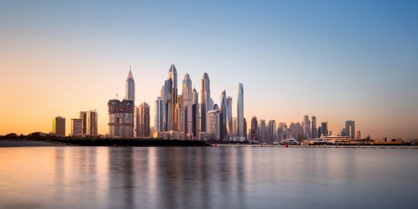 Sunset view of a modern city skyline with skyscrapers reflected in calm water.