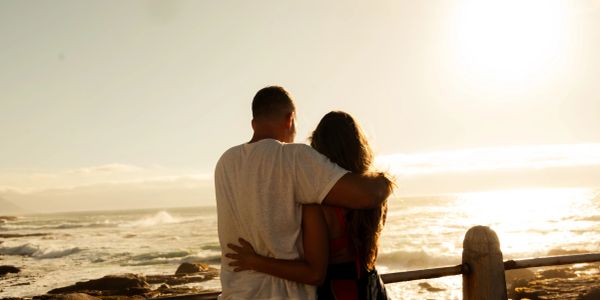 Couple embraces overlooking the ocean at sunset.