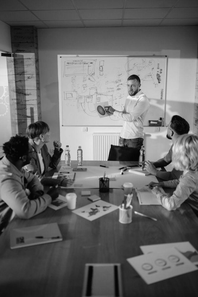 Black pencils in a gray holder next to a stack of white magazines with a camera in the background.