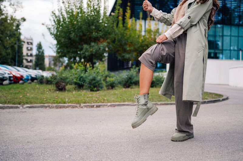 Fashionable woman is playfully lifting one leg while standing on a city street, showcasing her confidence and modern style