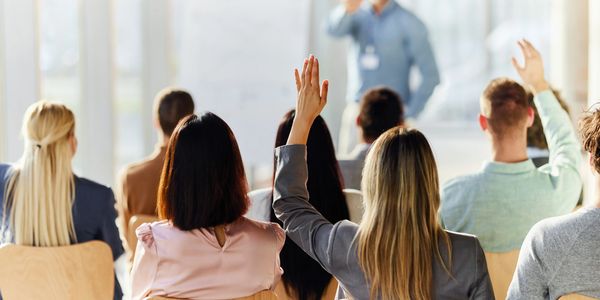 People raising hands in a classroom or seminar setting.