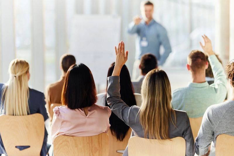 Rear view of a businesswoman raising her hand to ask a question on an education event in board room.