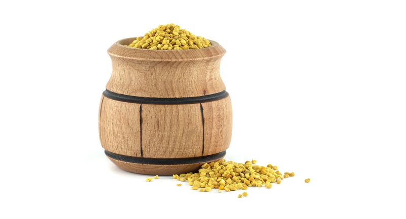Bee pollen in a rustic wooden container spilling on a white backdrop, symbolizing natural health and wellness benefits