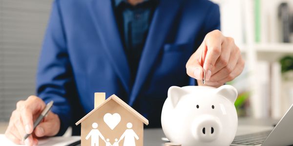 Person saving money in a piggy bank with a family house model nearby.