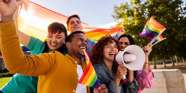 A joyful group celebrating with rainbow flags and a megaphone outdoors.