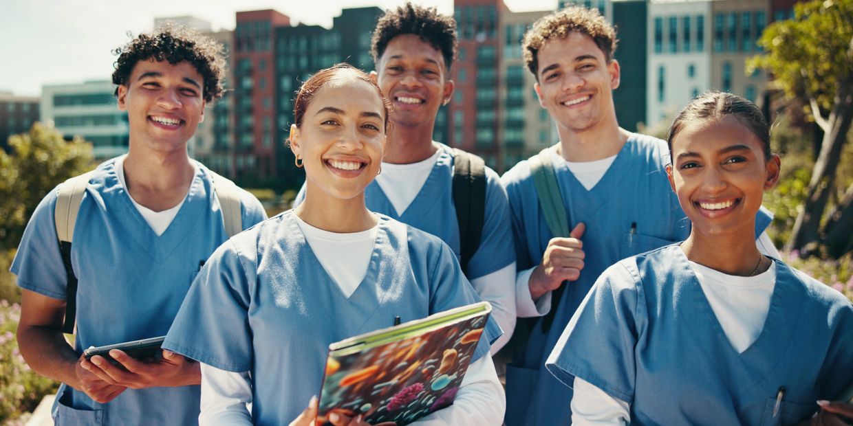 A group of smiling nursing students outdoors with books and backpacks.