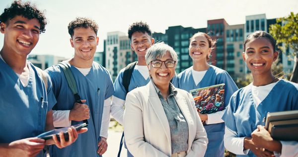 Group of smiling nursing students and a teacher outdoors.