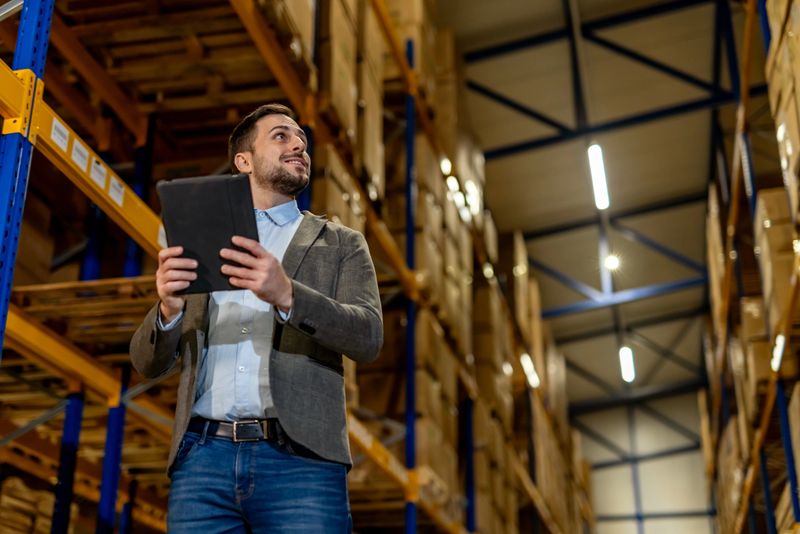 Professional manager examining inventory in a well-organized storage facility, using advanced technology for efficient operations. The image highlights modern business practices and logistical efficiency in a warehouse environment.