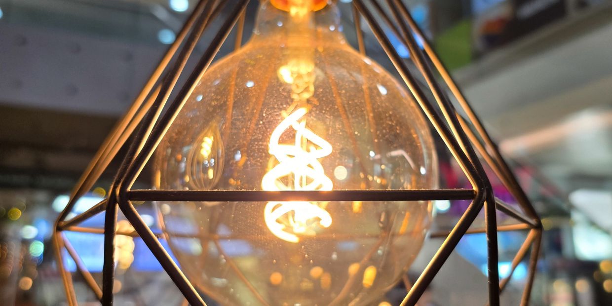 Close-up of a glowing vintage filament bulb in a geometric metal frame.
