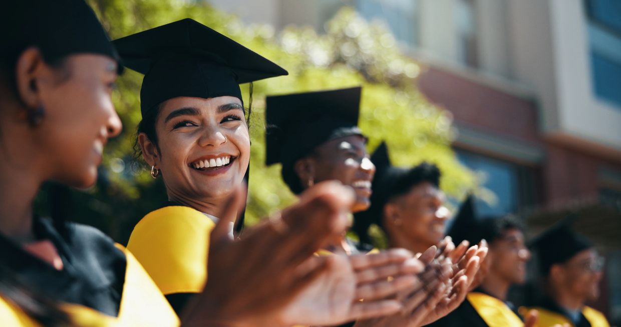 Happy graduates in caps and gowns clapping outdoors.