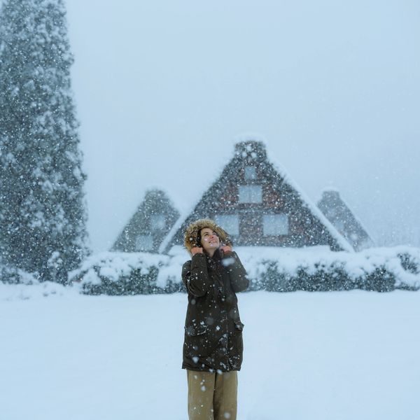 A person enjoys snowfall in front of snow-covered triangular houses.