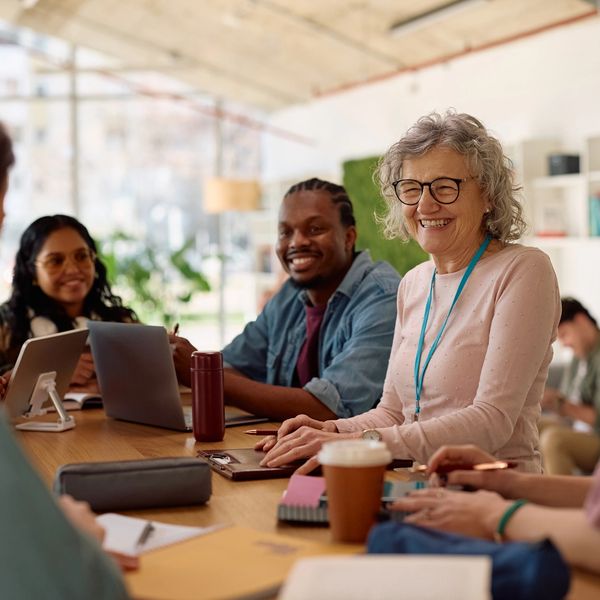 A diverse group of people happily collaborating around a table with laptops and notebooks.