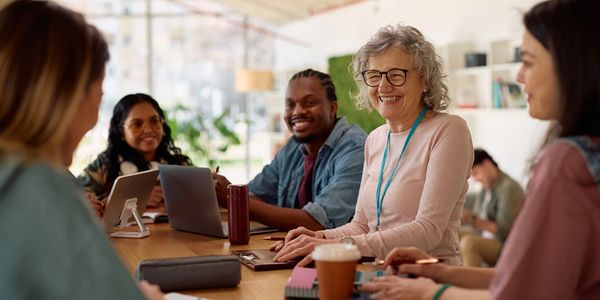 Group of adults smiling and working together at a table with laptops and coffee.
