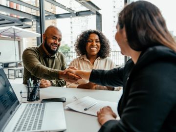 Two people shaking hands with a woman in an office.
