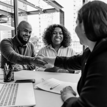 Two people shaking hands with a professional across a desk.