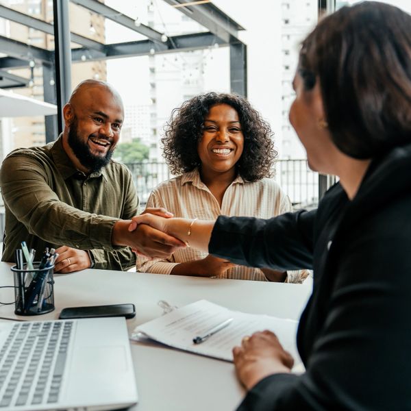 Couple smiling and shaking hands with a professional across a desk.