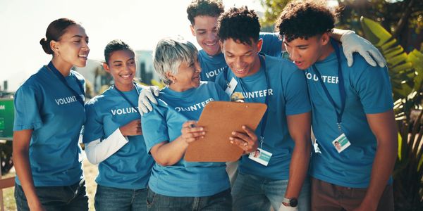 A diverse group of volunteers happily reviewing a clipboard outdoors.