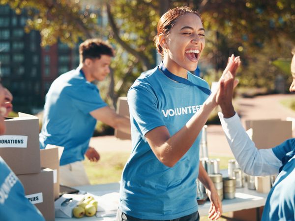 Volunteers in blue shirts enthusiastically high-five at an outdoor donation drive.