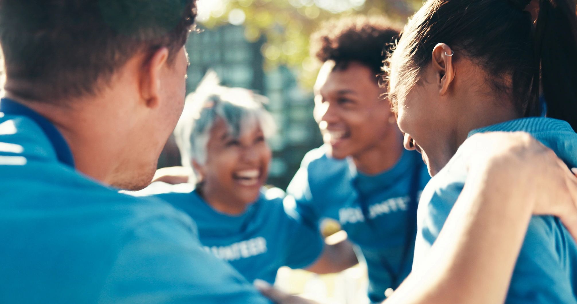Group of volunteers joyfully huddling outdoors in blue shirts.