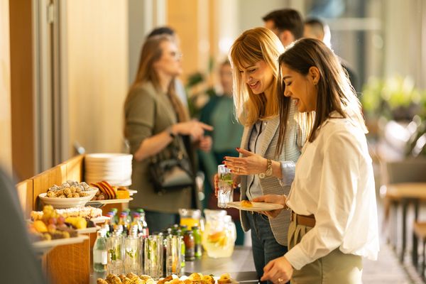 Two women enjoying a buffet with drinks and snacks at a social event.