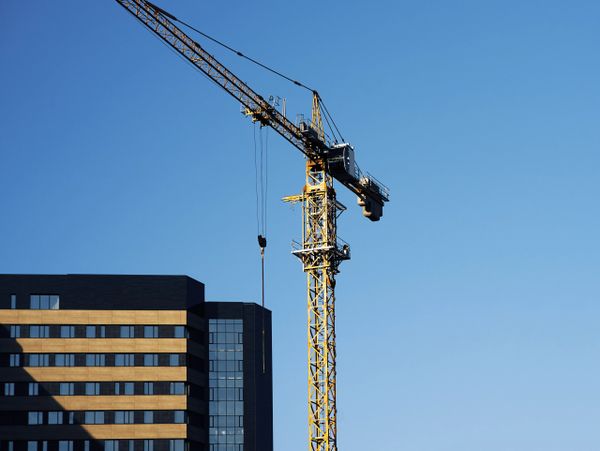 A tall yellow construction crane next to a modern building under clear blue sky.
