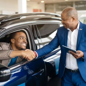 Car salesman shaking hands with a happy customer inside a car.
