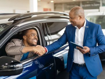 A man shakes hands with a car salesman inside a dealership.